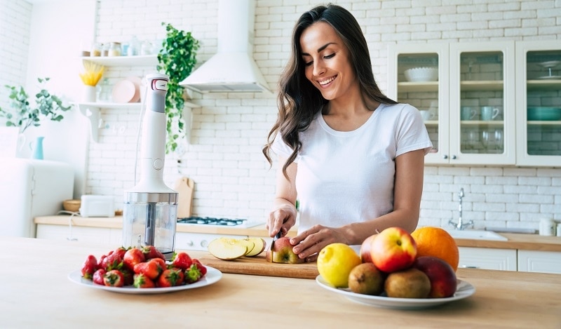 Smiling Woman Cutting Fresh Fruit in Kitchen to Follow Healthy Eating Diet | Vitacost.com/blog