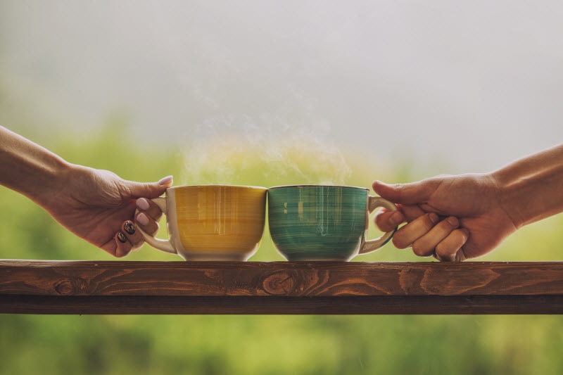 Two Hands Clinking Together Teacups on Wooden Table Outdoors to Represent Mindsight Technique of Tea Sitting | Vitacost.com/blog