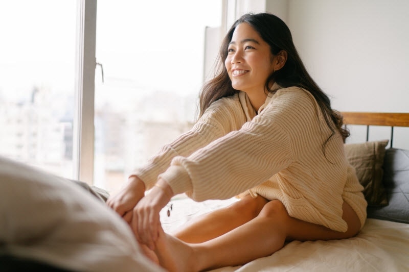Smiling Woman Stretching Legs in Bed After Learning New Facts About Joints & Arthritis | Vitacost.com/blog