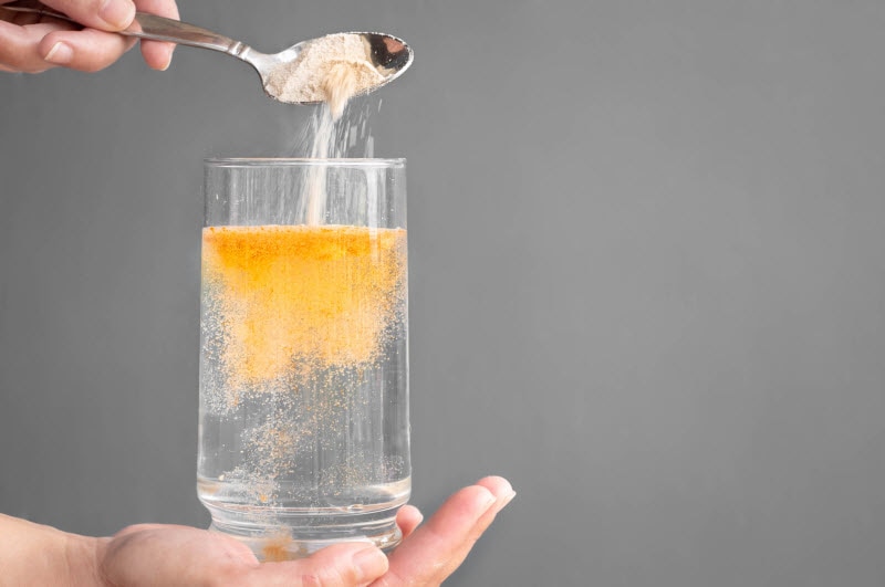 Woman Learning How to Restore Electrolytes Adding Orange Powder Supplement to Glass of Water | Vitacost.com/blog