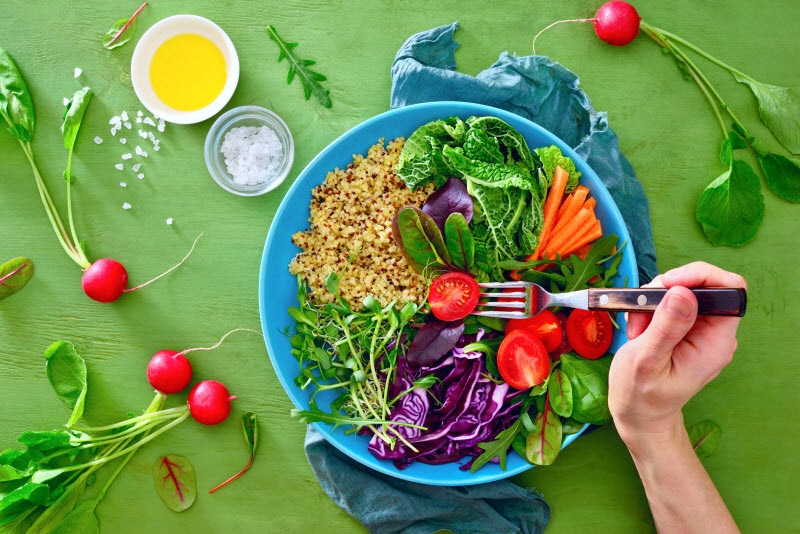 Person Forking Into a Colorful Salad on Green Surface After Switching to a Plant-Based Diet During the Pandemic | Vitacost.com/blog