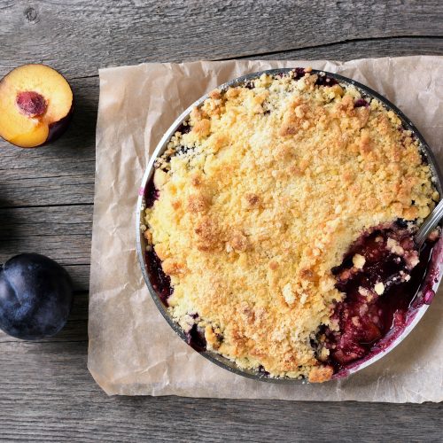 Top View of Plum Crumble with Spoon Sticking Out Next to Fresh Plums | Vitacost Blog