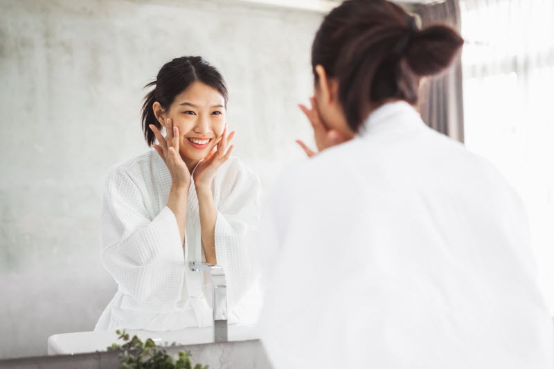 Woman Smiling in Mirror Because Probiotics Helped Her Gut Health and Skin Health | Vitacost.com/blog