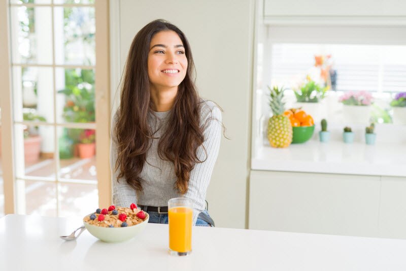 Smiling Woman Following Healthy Living Habits Eating Breakfast at Kitchen Counter | Vitacost.com/blog
