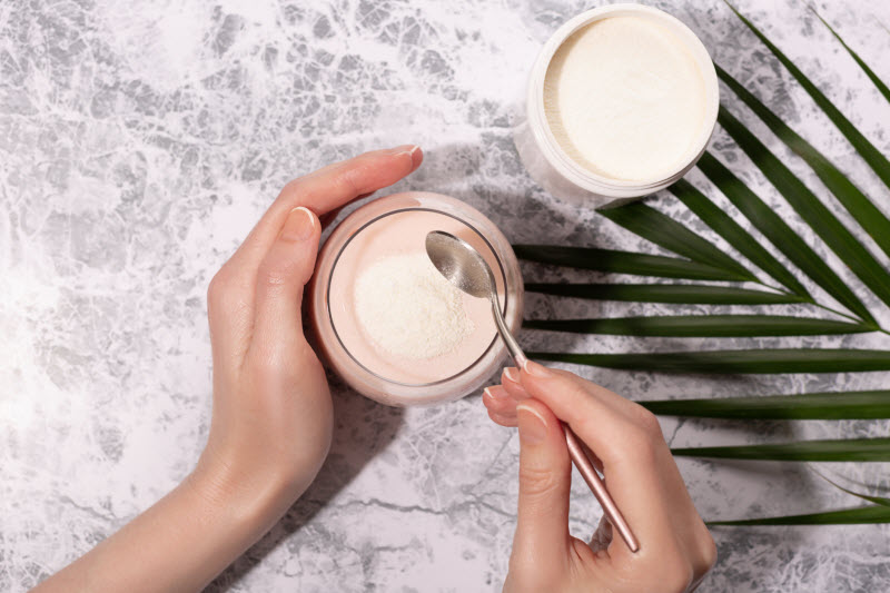 Woman's Hand Scooping Powder From Jar on Marbled Surface to Represent Question Can You Get Collagen from Plants? | Vitacot.com/blog