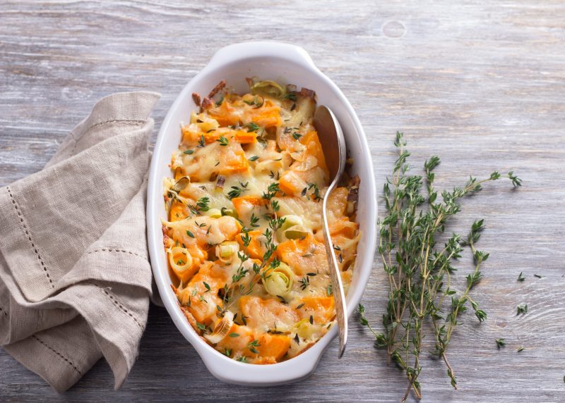 Top View Cheesy Pumpkin Pasta Bake in White Dish Next to Napkin and Green Garnish | Vitacost Blog