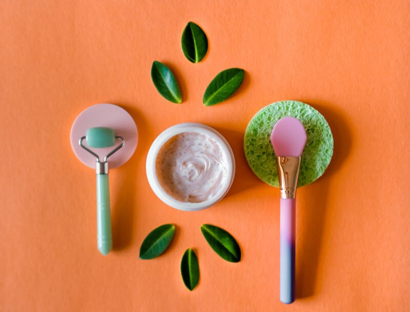 Beauty Tools and Cream with Green Leaves on Orange Solid Background | Vitacost.com/blog