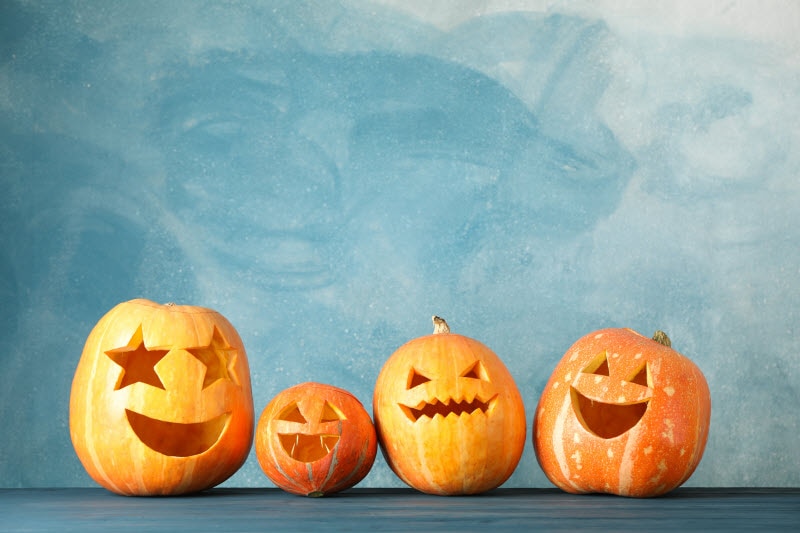 Four Festive Orange Jack o Lanterns on Slate Surface with Light Blue Background to Represent Fun Halloween Activities | Vitacost.com/blog