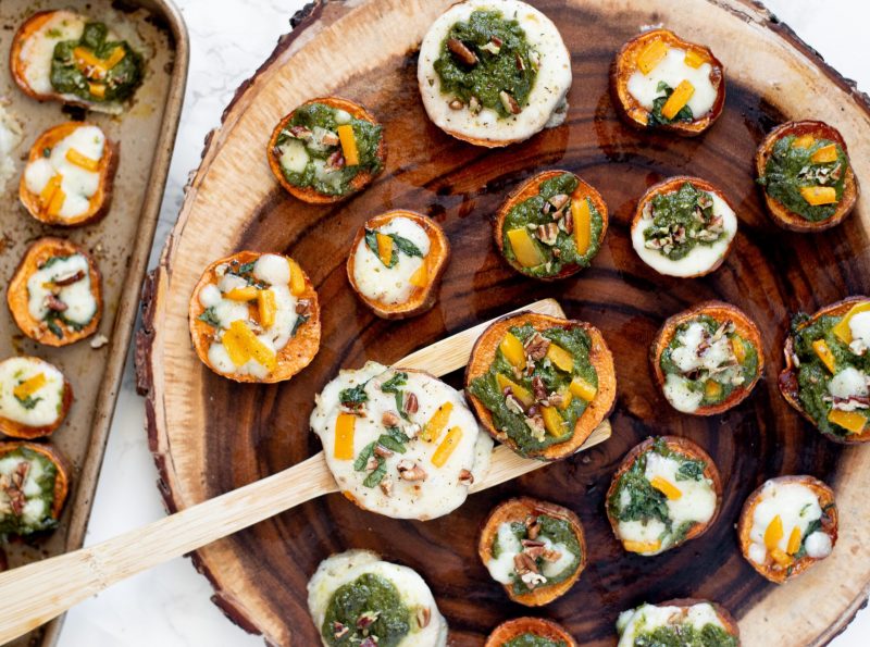 Wooden Spatula Holding Two Roasted Sweet Potato Pizza Bites over Cut of Wood Covered in More Bites | Vitacost Blog