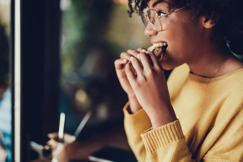 Side View of Woman in Yellow Sweater Taking Bite of one of the Best Foods for Mental Health | Vitacost.com/blog