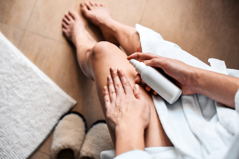 Woman Enjoying Magnesium Oil Benefits While Spraying Topical Magnesium on Legs After Bath | Vitacost.com/blog