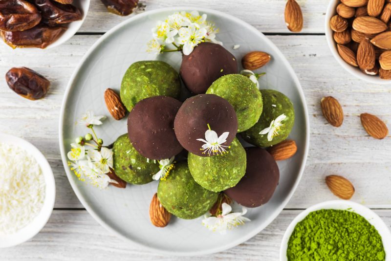 Green and Chocolate-Coated Matcha Balls on White Plate Surrounded by Almonds, Matcha Powder and Flowers | Vitacost Blog