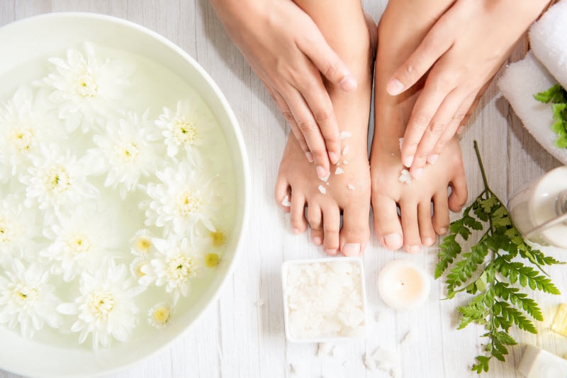 Foot Spa Scene with Soaking Bowl Filled with Flowers and Foot Massage Oil Beside Woman's Feet | Vitacost.com/blog