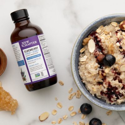 Bottle of New Chapter Elderberry Syrup Between Bowl of Oatmeal, Spoon with Syrup and Honey | Vitacost Blog