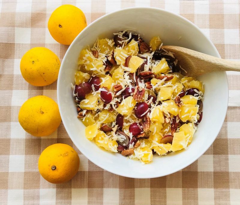 Top View Oranges Pieces and Grapes in Bowl Topped with Pecans and Coconut Shreds Next to Fresh Oranges On Checkered Cloth | Vitacost Blog