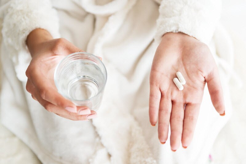 Woman Taking Supplements Holding Glass of Water in One Hand and Capsules in the Other | Vitacost.com/blog