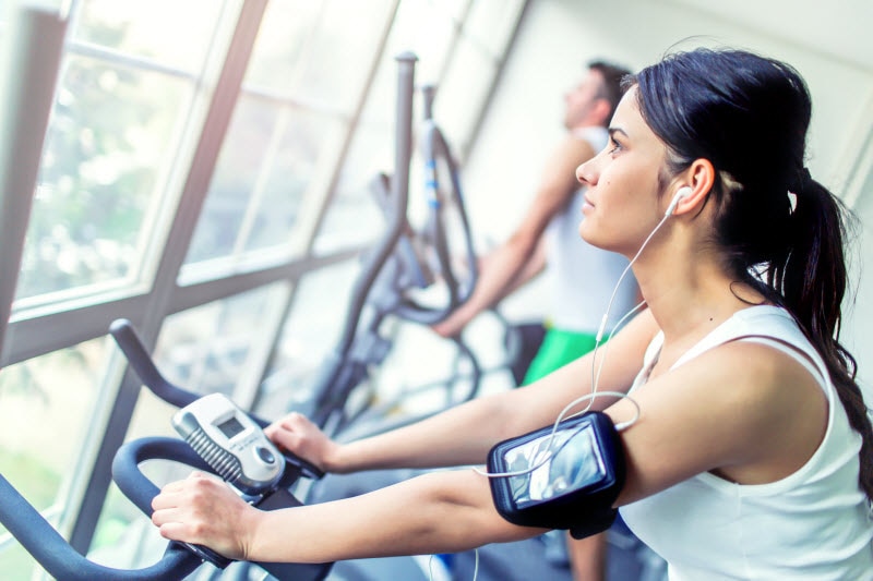 Does Exercise Help Anxiety? 3 Ways Moving More Benefits Mental Health Side View of Woman on Fitness Bike Peering Out Window Wondering About Exercise and Anxiety | Vitacost.com/blog