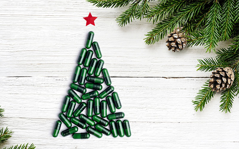 Green Supplements in Tree Shape With Red Star on White Wood Surface to Represent Holiday Health Tips | Vitacost.com/blog