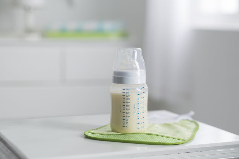 Ways to Reduce Microplastics Exposure With Baby Bottle Use Baby Bottle on Green Bib on Kitchen Counter to Represent Ways to Reduce Microplastics Exposure | Vitacost.com/blog