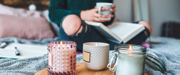 Woman Trying to Boost Mental Health Sitting in Cozy Bed With Book and Mug of Tea with Relaxing Candles | Vitacost.com/blog