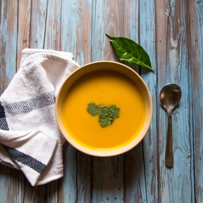 Top View Butternut Squash Soup on Blue Wood Next to Napkin, Spoon and Green Garnish | Vitacost Blog