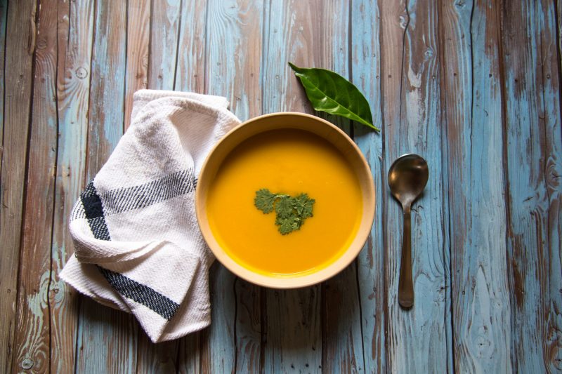 Top View Butternut Squash Soup on Blue Wood Next to Napkin, Spoon and Green Garnish | Vitacost Blog