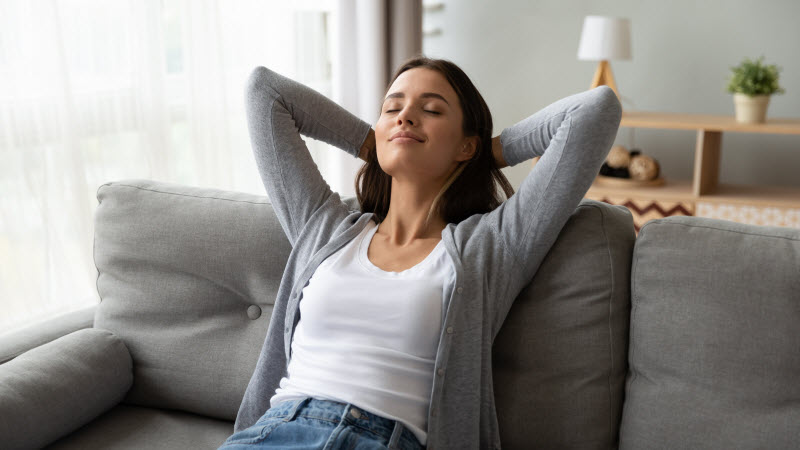 Woman Who Learned How to Unplug Relaxing on Sofa with Eyes Closed and Arms Behind her Head | Vitacost.com/blog