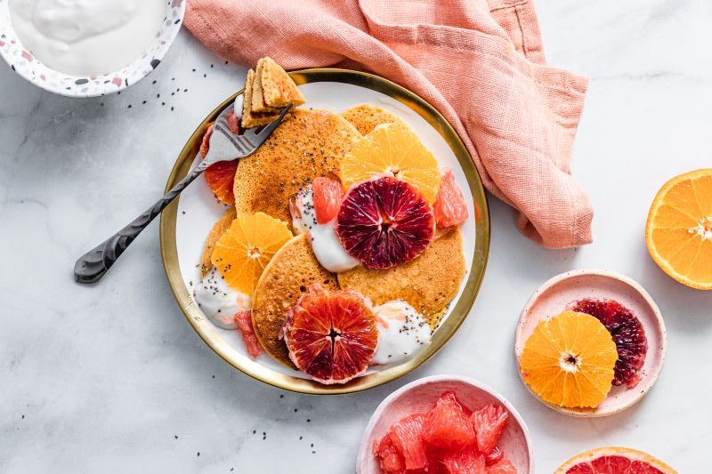 Citrus-Infused Gluten-Free Pancake Recipe on Stoneware Plate with Orange Slices, Dairy-free Yogurt, Honey and Chia Seeds | Vitacost.com/blog