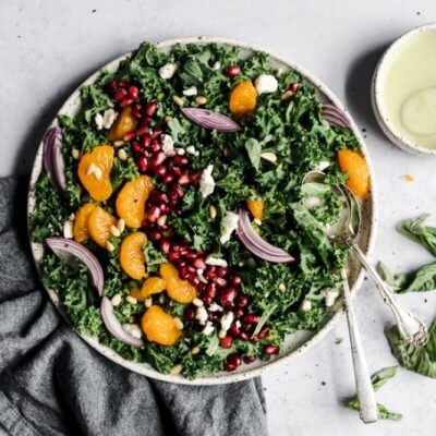 Kale Citrus-Pomegranate Salad with Basil Vinaigrette in Serving Bowl on White Countertop with Linen Napkin | Vitacost.com/blog