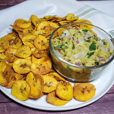 Pineapple Guacamole in Glass Bowl Surrounded by Air Fried Plantain Chips on White Plate Wood Table | Vitacost Blog