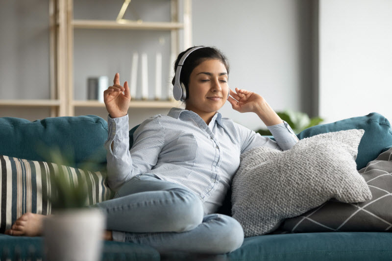 Woman Who is a Highly Sensitive Person Sitting on Couch Listening to Music With Headphones | Vitacost.com/blog