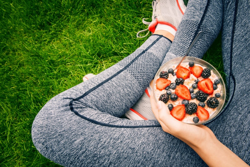 Woman Who Learned What to Eat Before Running with Bowl of Oatmeal and Berries in Lap | Vitacost.com/blog