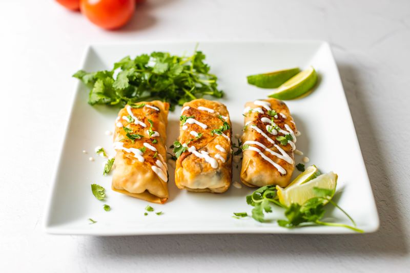 Southwest Baked Egg Rolls with Cilantro and Limes on White Plate with Drizzle of Sour Cream | Vitacost.com/blog