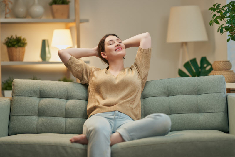 Woman Learning How to Practice Mindfulness Sitting on Couch with Arms Behind Head and Eyes Closed | Vitacost.com/blog
