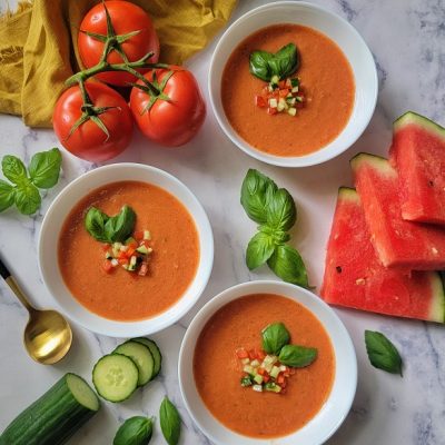 Three Bowls of Gazpacho Soup Garnished with Diced Vegetables and Sprigs of Basil