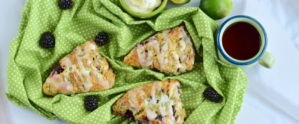 Three Blackberry Scones with Glaze on Green Cloth Surrounded by Blackberries, Cut Lime, Tea and Cream to Represent Blackberry Scone Recipe | Vitacost.com/Blog
