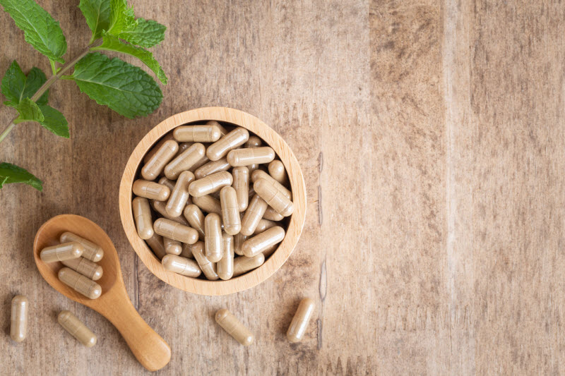 Concept of Herb Side Effects Represented by Wooden Bowl and Spoon With Herbal Capsules on Wood Surface | Vitacost.com/blog