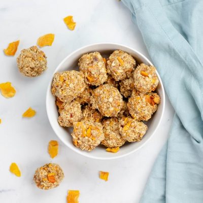 Oatmeal Energy Balls with Mango in a White Bowl Surrounded by Dried Mango Pieces and Two Energy Balls | Vitacost.com/Blog