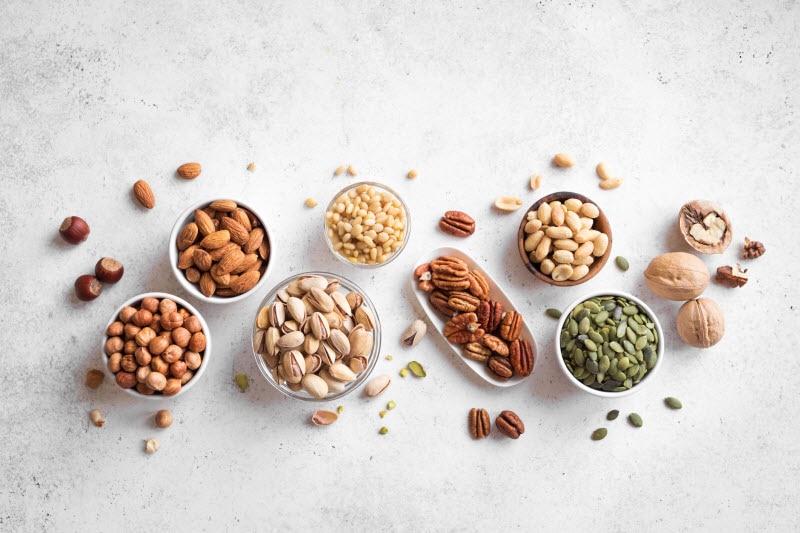 Overhead View of Bowls of Assorted Nuts on White Marbled Surface to Represent Anti-Nutrients Concept | Vitacost.com/blog