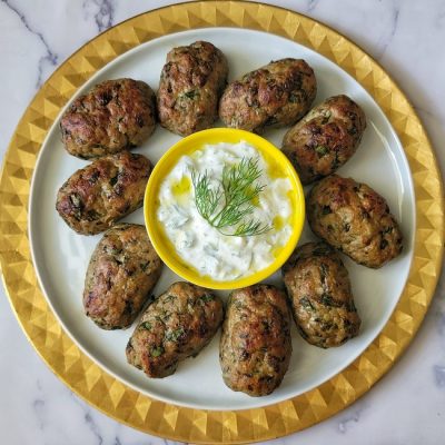 A Large White Plate With a Yellow Border is Topped With Nine Mini Turkey Meatloaves With a Small Bowl of Homemade Tzatziki Sauce to Represent Turkey Meatloaf Recipe | Vitacost.com/Blog