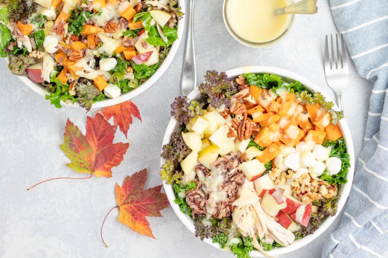 Fall Harvest Bowl Salad With Sweet Potato & Kale in Two Bowls Next to Autumn Leaves on Table Top | Vitacost.com/blog