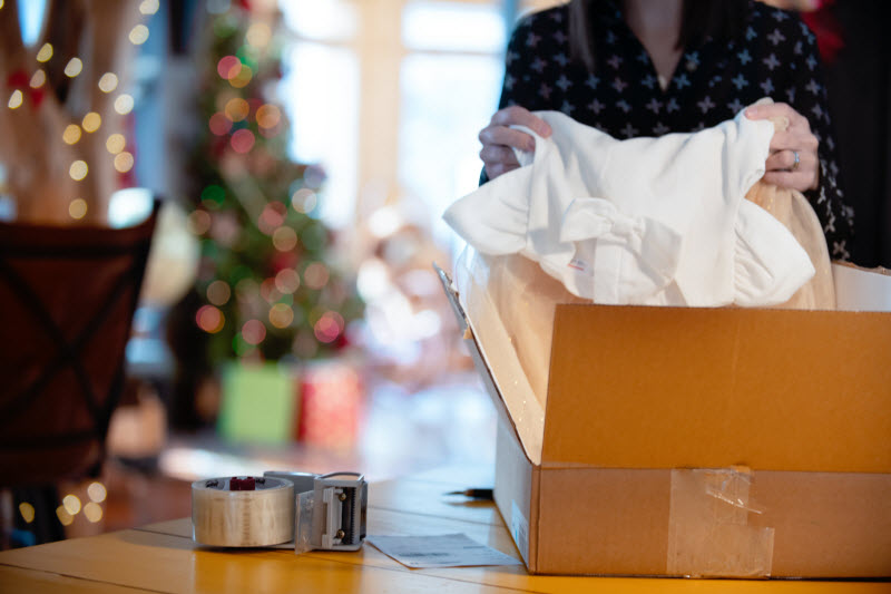 Holiday Recycling Concept Represented by Woman Opening Package on Table Beside Christmas Tree | Vitacost.com/blog