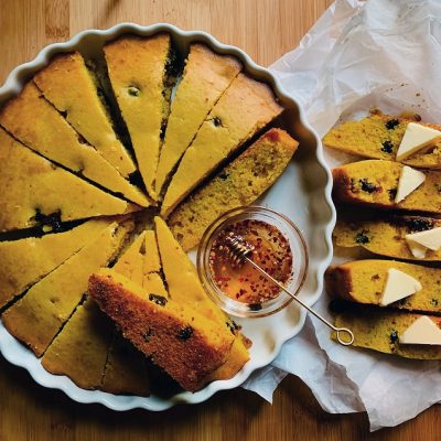 A Round Cornbread With Cranberries is Sliced into Wedges With a Small Bowl of Spicy Honey to Represent a Cornbread Recipe | Vitacost.com/Blog