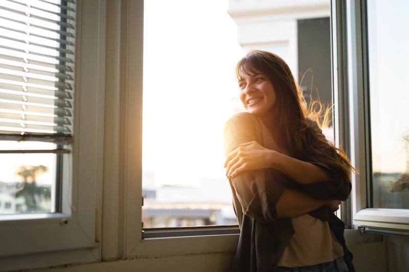 Woman Smiling Looking Out Open Window as She Reflects on Cutting Back on Drinking | Vitacost.com/blog
