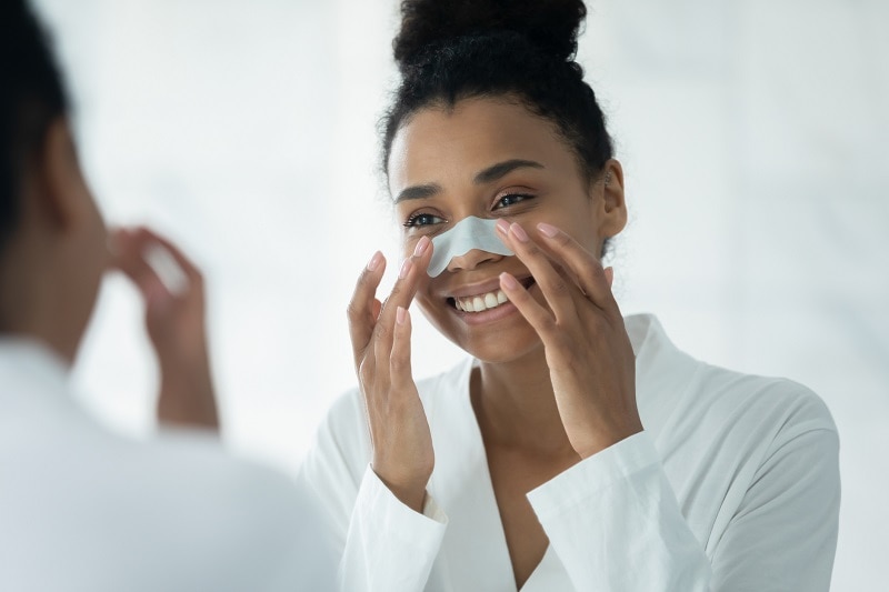 A Young Woman Applies a Blackhead Removal Strip to Represent What Are Blackheads | Vitacost.com/Blog