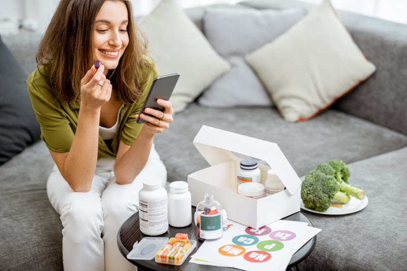 9 Cleanse and Detox Kits to Help You Refresh in 2022 Smiling Woman Reviewing Supplements and Literature in Cleanse and Diet Kit Sitting on Gray Couch | Vitacost.com/blog