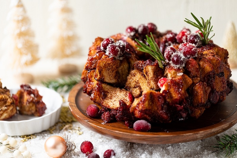 Homemade Cranberry-Glazed Monkey Bread Garnished with a Rosemary Sprig on Cake Stand | Vitacost.com/Blog