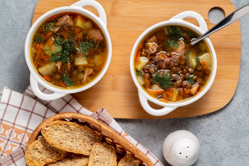 Hearty Chicken and Lentil Soup in Two Bowls Next to Plate of Bread on Gray Counter | Vitacost.com/blog