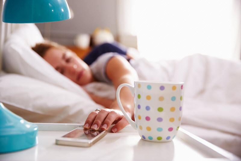 Woman Taking a Coffee Nap Hitting Snooze on Phone Alarm Beside Polka-Dotted Mug | Vitacost.com/blog