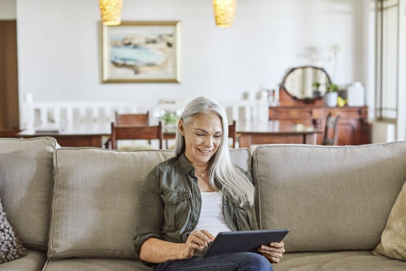 Concept of Can Loneliness Cause Heart Problems Represented by Woman on Couch Looking at Tablet | Vitacost.com/blog